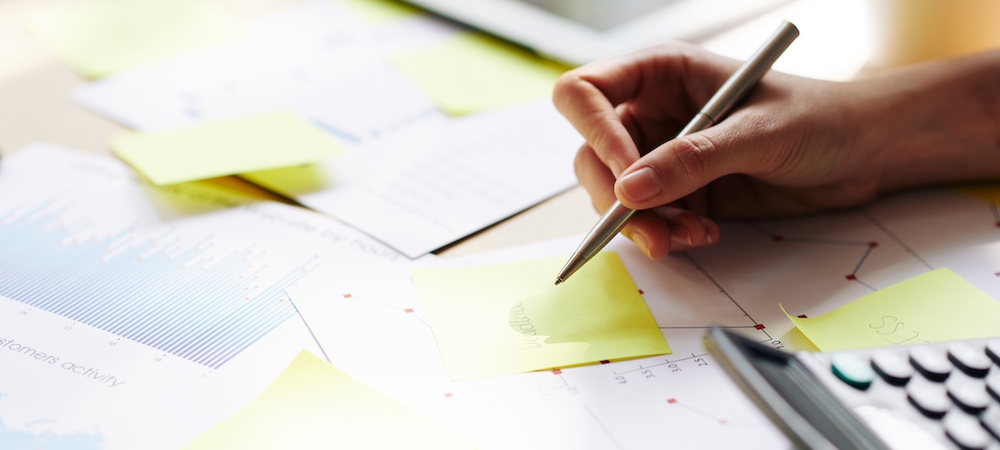 Hand Holding Pen Over Post-its and Calculator