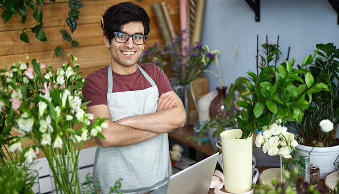 Small floral shop owner shows he is ready to serve your as he poses in his own flower shop.