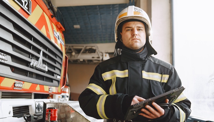 Firefighter in Uniform Holding Tablet and Standing in Front of Firetruck