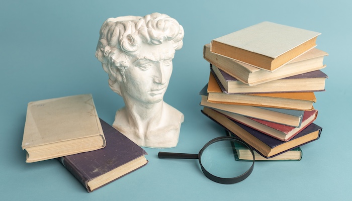 Statue of Bust Next to Stacked Books and Magnifying Glass