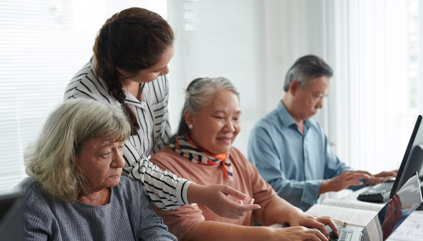 Older Adults Seated On Computers Being Taught by Standing Instructor