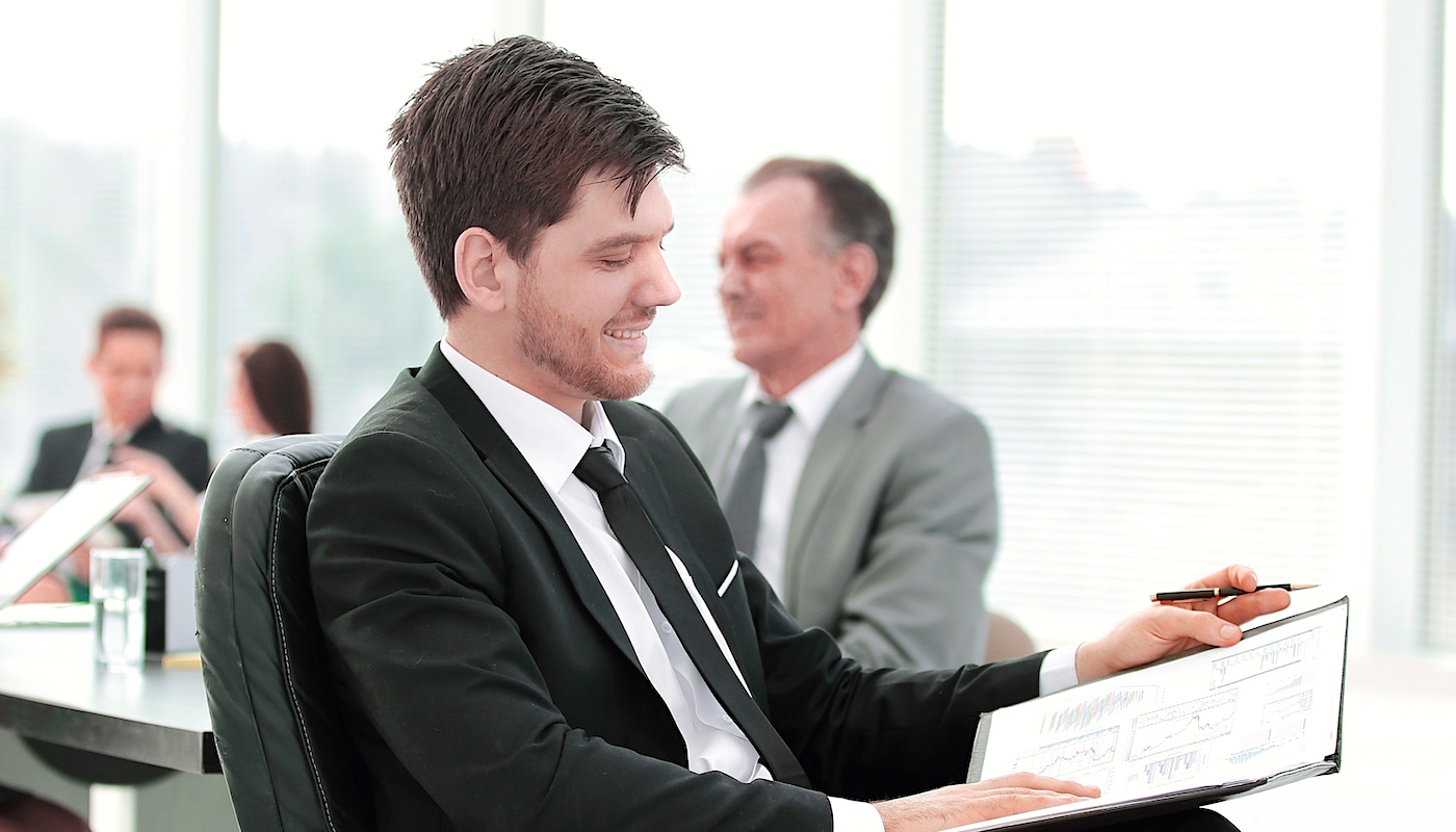 Man in Suit Looking Down and Smiling at Clipboard