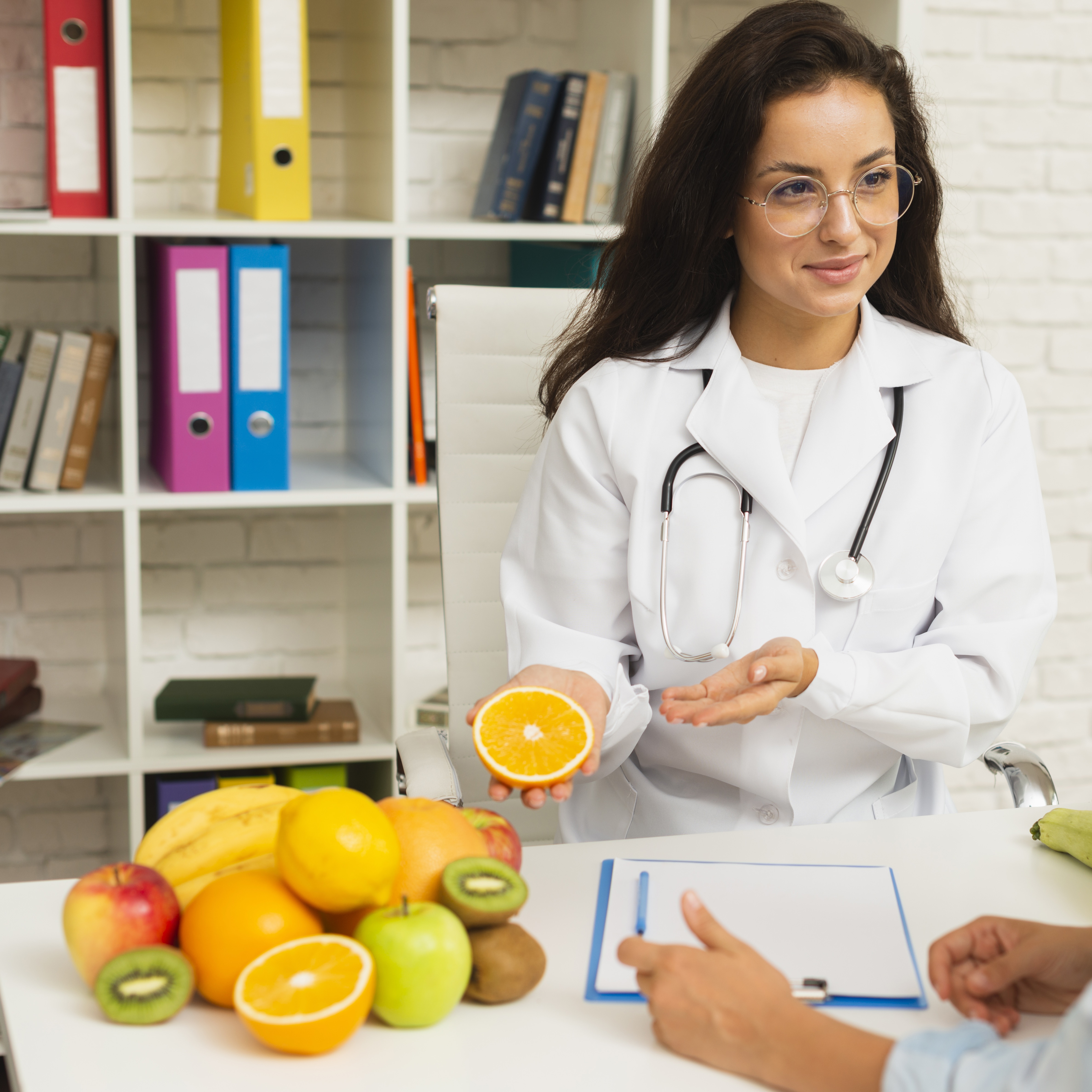 Nutritionist Holding Orange with other Fruits on Table Speaking with Patient