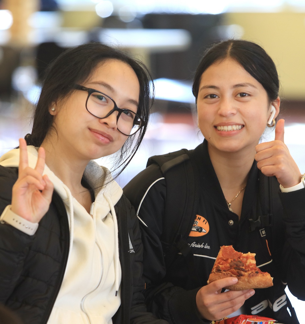 Two students posing for camera at first year experience orientation eating pizza